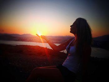 Optical illusion of woman holding sun against sky during sunset