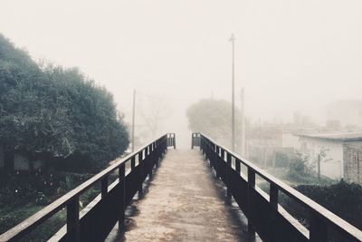 Empty footbridge against sky during foggy weather