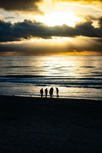 Silhouette people at beach against sky during sunset