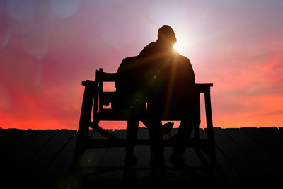 Silhouette couple sitting on seat against sky during sunset