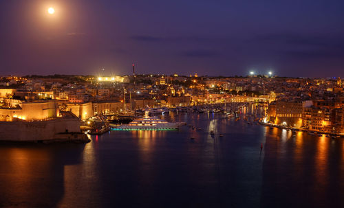 Illuminated city by sea against sky at night