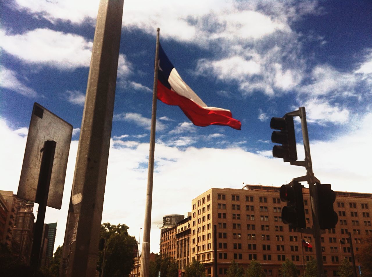 flag, building exterior, patriotism, national flag, architecture, low angle view, built structure, identity, sky, american flag, cloud - sky, city, cloud, tower, day, tall - high, wind, culture, outdoors, pole