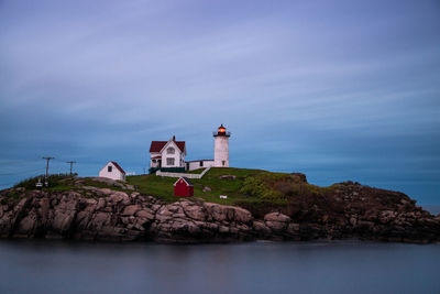 Lighthouse by sea against buildings and sky