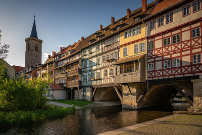 Arch bridge over river amidst buildings against sky in city