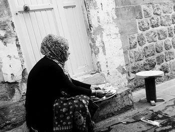 Side view of woman sitting against wall