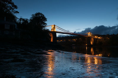 View of suspension bridge over river at sunset