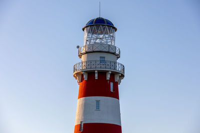 Lighthouse in red and white colors on the seashore, river bank or lake shore.