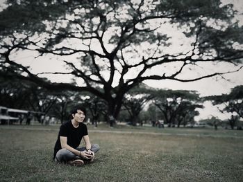 Thoughtful man sitting on grassy field against trees at park