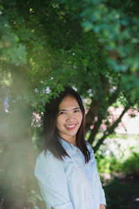 Portrait of a smiling young woman standing against trees