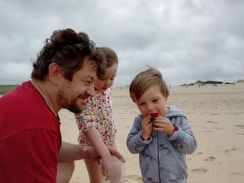 Grandpa sharing strawberries with kids on a beach.