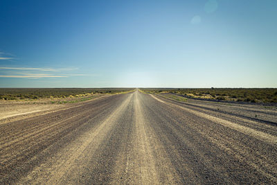 Empty road amidst field against sky