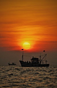 Silhouette ship in sea against orange sky