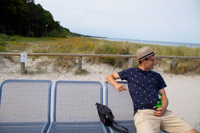 Young man having drink on chair at beach