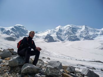 Man sitting on rock by snowcapped mountain against sky