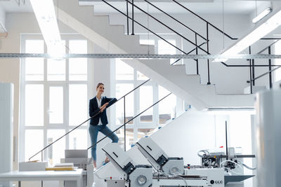 Female business professional leaning on railing in workshop