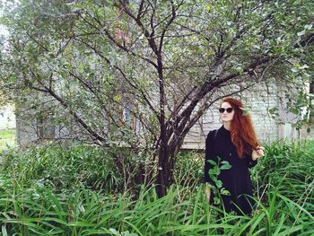 Portrait of young woman standing by tree against sky