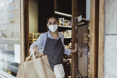 Portrait of female owner with take away food at doorway of delicatessen shop