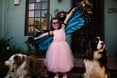 Young girl in dress up standing on porch with dogs