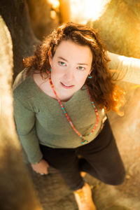 High angle portrait of smiling woman standing by tree trunk