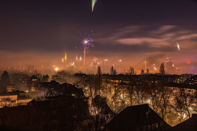 Firework display over city against sky at night