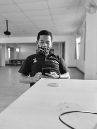 Portrait of man holding camera while sitting on table