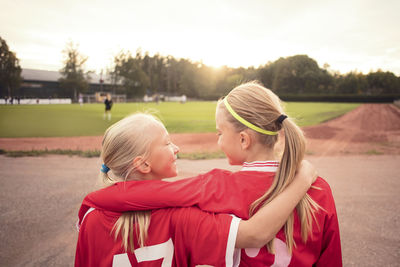 Rear view of happy female athletes looking at each other standing on footpath during sunset