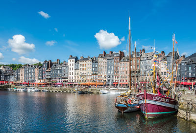 Sailboats moored on river by buildings against sky