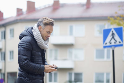 Mature man using smart phone against building