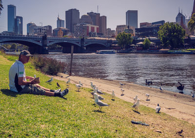 People sitting by river in city against sky