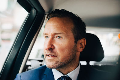 Mature businessman looking away while sitting taxi in city