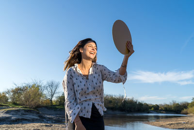 Smiling young woman standing against sky