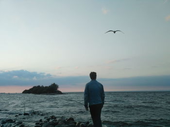 Rear view of man standing at beach during sunset