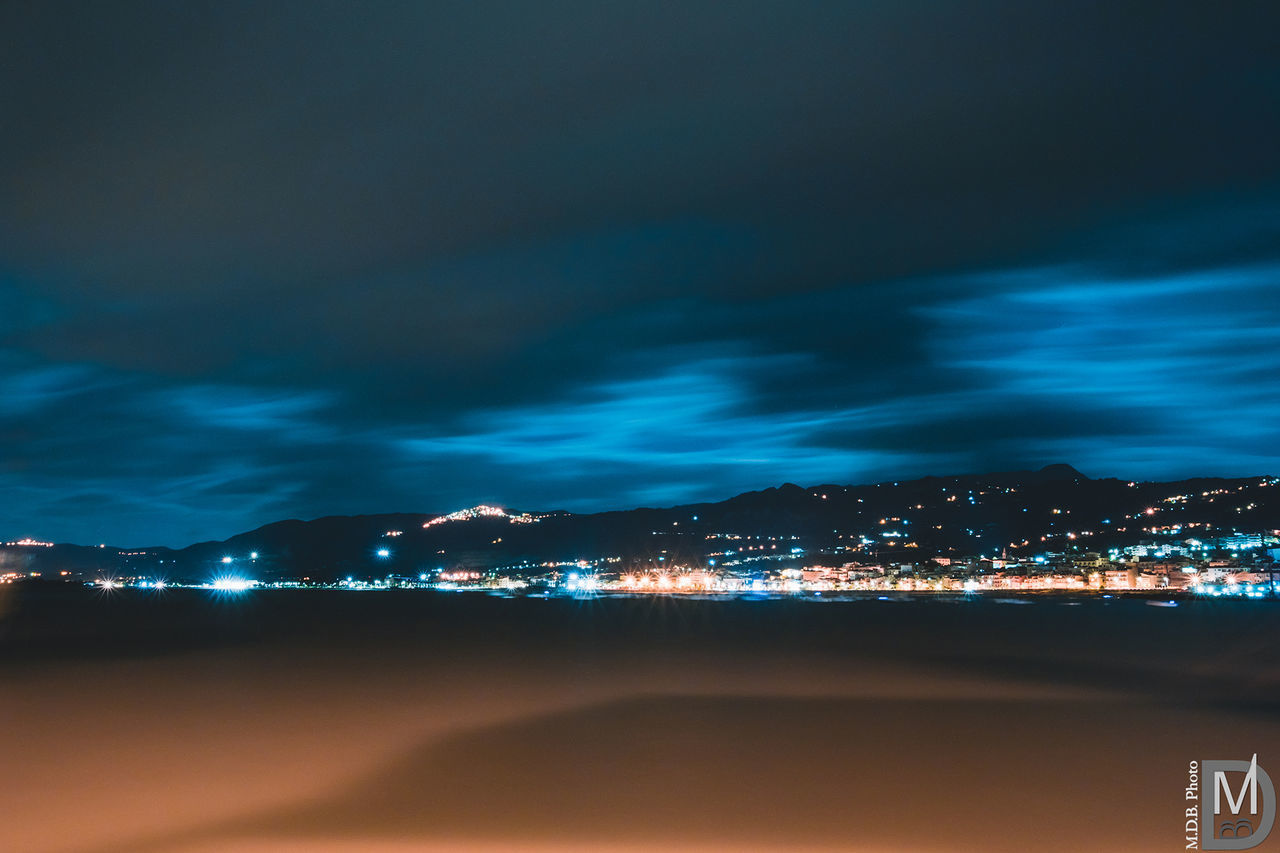 ILLUMINATED CITYSCAPE BY SEA AGAINST SKY