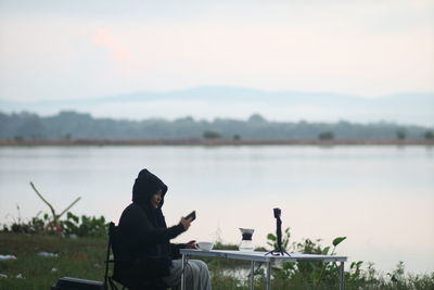 Rear view of man sitting by lake against sky