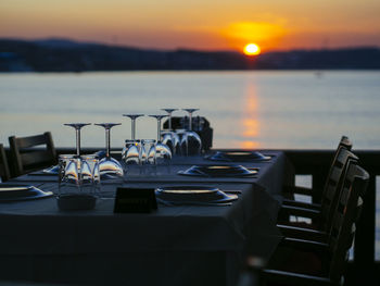 Chairs and table by sea against sky during sunset