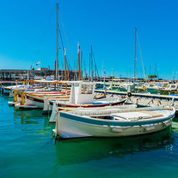 Boats moored at harbor against clear blue sky