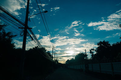Silhouette electricity pylon by road against sky during sunset