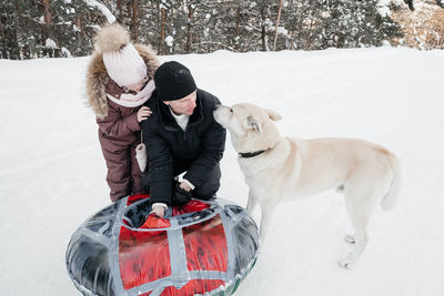 Dad and daughter are preparing sleds for skiing, the dog is playing