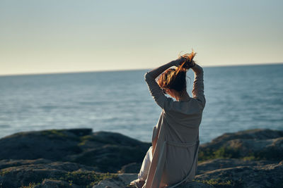 Woman holding umbrella at sea shore against sky during sunset