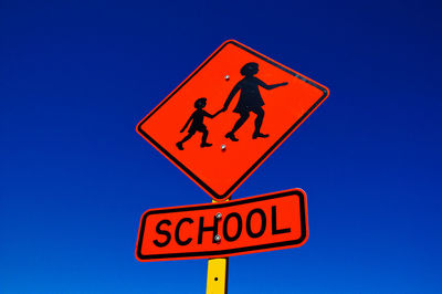 Low angle view of school crossing sign against clear blue sky