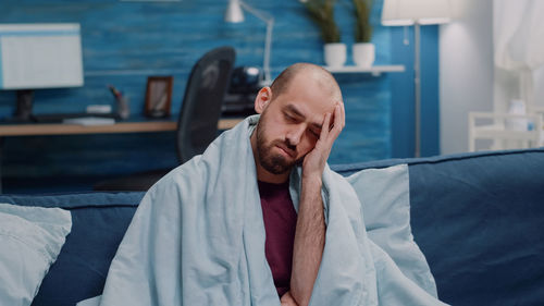 Young man looking away while sitting on bed