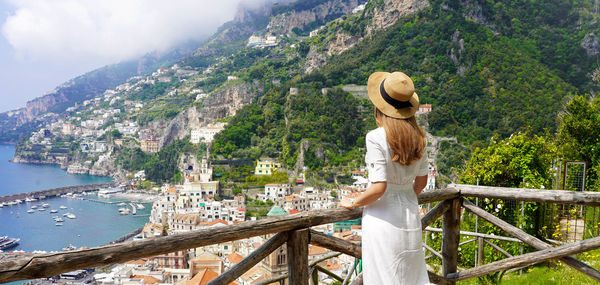 Peaceful woman with white dress and hat enjoying landscape from terrace on amalfi coast, italy