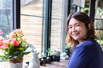 Portrait of smiling woman with flowers against window