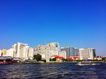 Sea by cityscape against clear blue sky