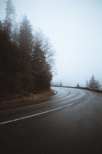 Empty road by trees against sky