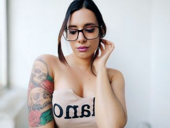 Portrait of young woman wearing eyeglasses standing against wall