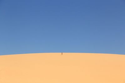 Mid distance view of person standing in desert against clear blue sky