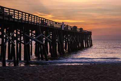 Wooden posts on beach against sky during sunset