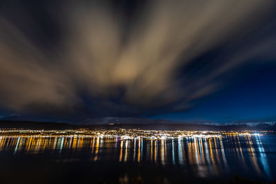 Illuminated city by sea against sky at night