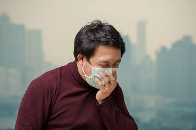 Asian man wearing the face mask against air pollution with coughing at the balcony of high apartment
